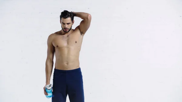 Homem esportivo em shorts segurando garrafa de esportes azul perto da parede de tijolo branco — Fotografia de Stock