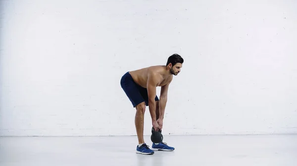 Bärtiger und sportlicher Mann, der mit schwerer Kettlebell nahe der weißen Ziegelwand trainiert — Stockfoto