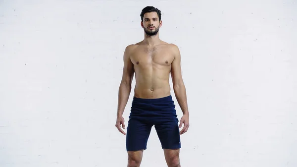 Shirtless sportsman in shorts standing near white brick wall — Stockfoto