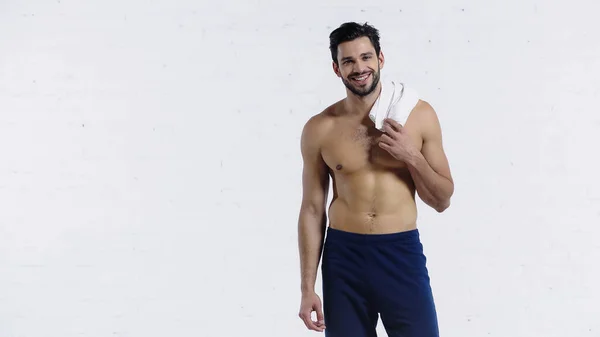 Веселый спортсмен, держащий полотенце и смотрящий на камеру возле белой кирпичной стены — стоковое фото