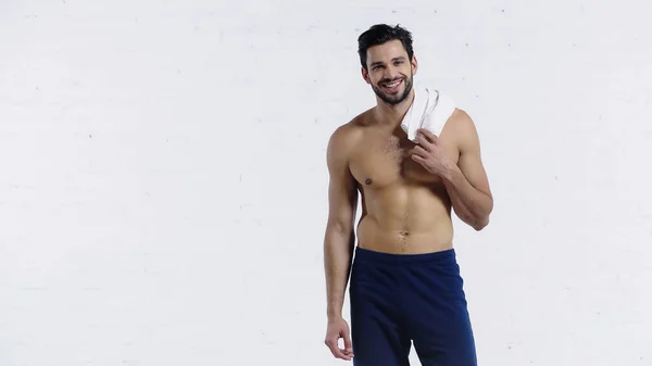 Desportista alegre segurando toalha e olhando para a câmera perto da parede de tijolo branco — Fotografia de Stock