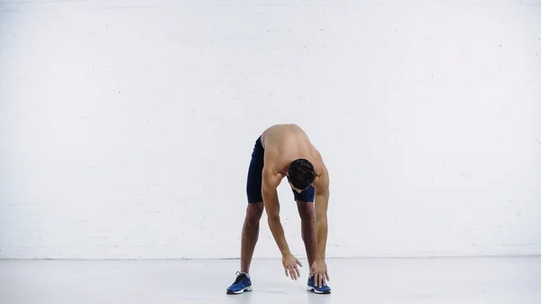 Shirtless man doing forward leaning near white brick wall — стоковое фото