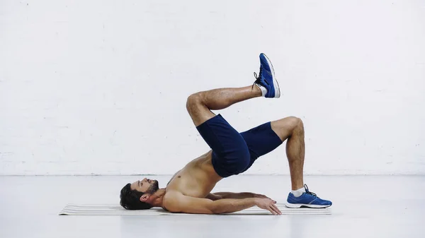Вид сбоку тренировки спортсмена без рубашки на фитнес-коврике возле стены из белого кирпича — стоковое фото