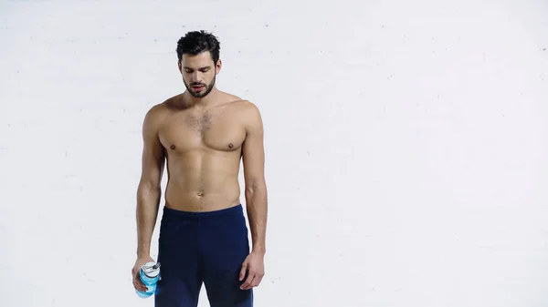 Desportista muscular em calções azuis segurando garrafa de esportes perto da parede de tijolo branco — Fotografia de Stock