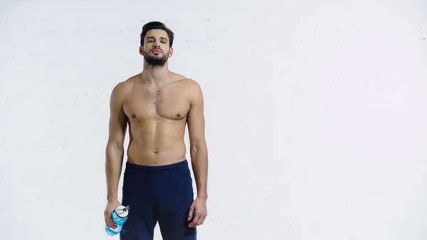 Sportlicher Mann in blauen Shorts mit Sportflasche in der Nähe weißer Backsteinmauer — Stockfoto