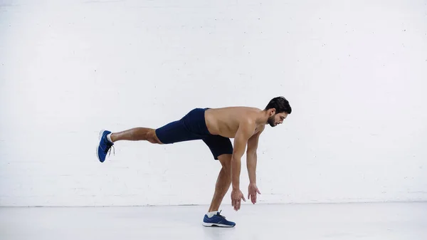 Side view of shirtless sportsman doing forward leaning near white brick wall — стоковое фото