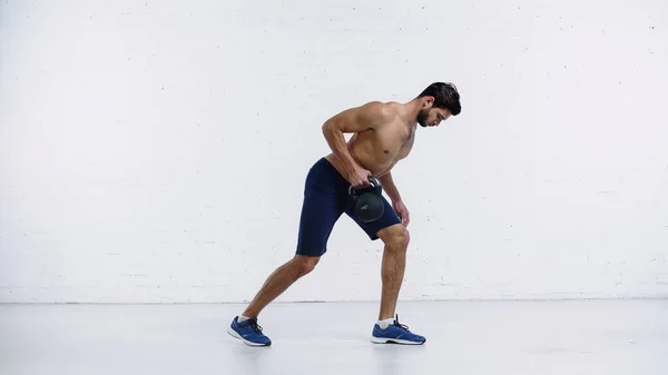 Deportista en zapatillas de deporte haciendo ejercicio con pesadas pesas cerca de la pared de ladrillo blanco - foto de stock