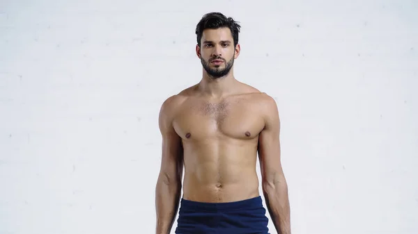 Hemdloser und sportlicher Mann blickt nahe weißer Ziegelwand in die Kamera — Stockfoto