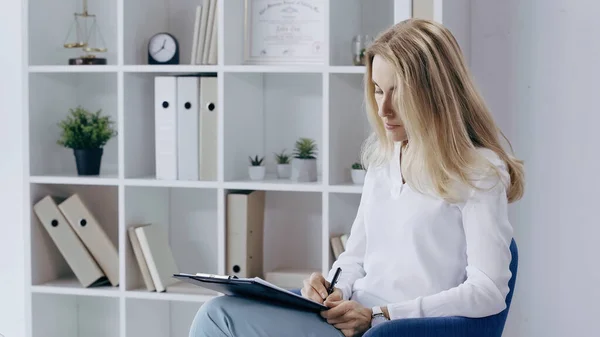 Concentrated psychologists writing on clipboard near rack in consulting room — Fotografia de Stock