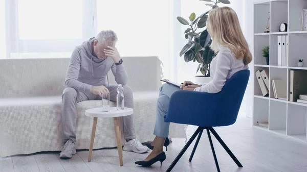 Depressiver reifer Sportler und blonder Psychologe unterhalten sich im Sprechzimmer — Stockfoto