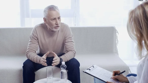 Middle aged man sitting on sofa and talking with psychotherapist — Stock Photo