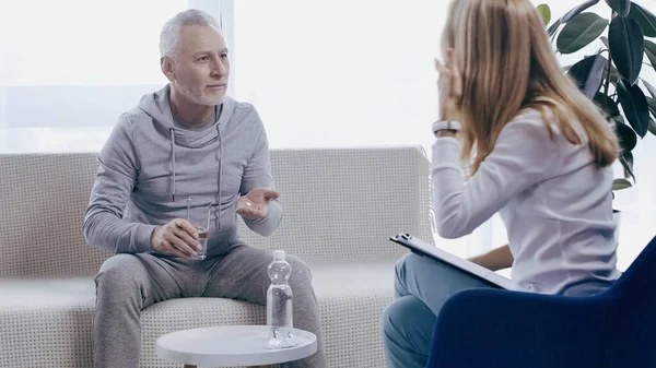 Mann mittleren Alters in Sportbekleidung nimmt Tablette in der Nähe eines Psychotherapeuten — Stockfoto