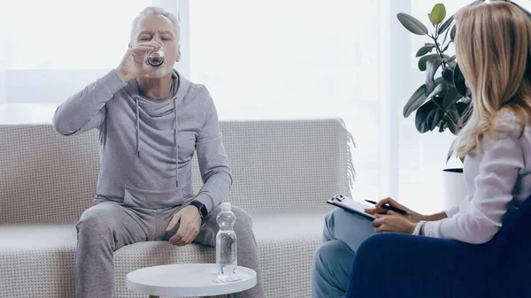 Middle aged man in sportswear drinking water near psychotherapist — Foto stock