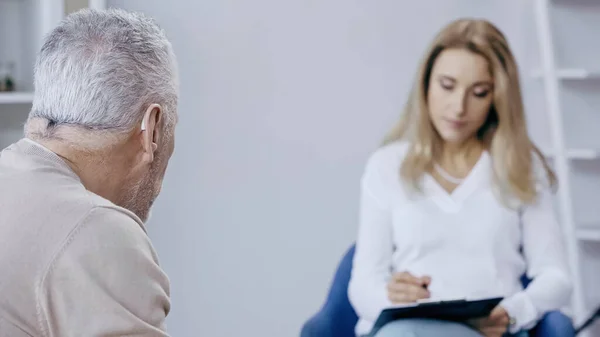 Hombre de mediana edad cerca de psicoterapeuta borrosa - foto de stock