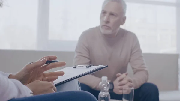 Psychologue tenant presse-papiers près homme flou dans la salle de consultation — Photo de stock