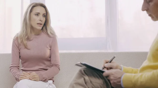 Mujer rubia hablando durante la consulta con psicólogo borroso - foto de stock