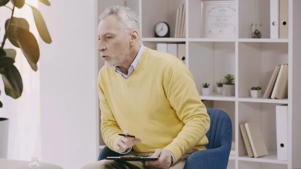 Mature psychologist talking while holding clipboard during consultation — Stockfoto