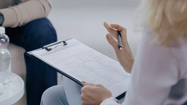 Cropped view of psychologist holding pen and clipboard in consulting room — Stock Photo