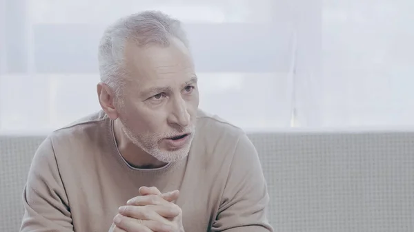 Upset mature man talking in consulting room during psychotherapy — стоковое фото