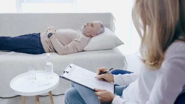 Блондинка-психолог тримає кишеню біля пустотливого чоловіка середнього віку, який лежить на дивані під час терапії — стокове фото