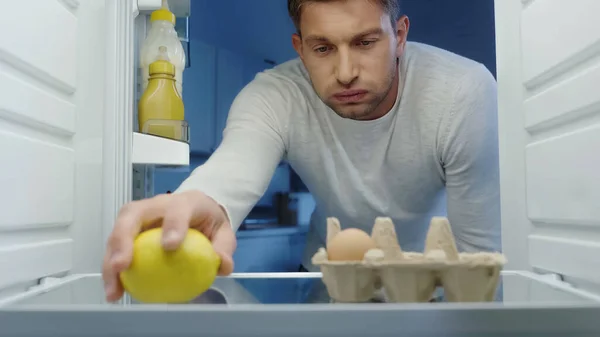 Displeased man puffing cheeks while taking lemon from refrigerator — Stock Photo