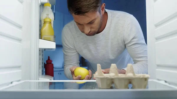 Upset man holding egg and lemon near refrigerator with sauces — Stock Photo