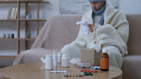 Selective focus of medicaments on table near sick man reading medication instruction on blurred background — Stock Photo