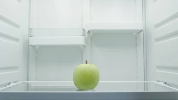 Whole fresh apple on shelf in empty refrigerator — стоковое фото