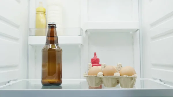 Botella de cerveza, leche, huevos y salsas en nevera - foto de stock