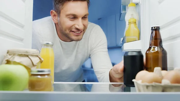 Happy man taking soda from fridge near bottle of beer, orange juice, eggs, and jars with food — Fotografia de Stock