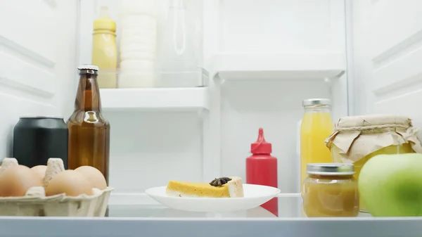 Tasty cake, eggs, apple, bottles with drinks, sauces, honey and fruit puree in refrigerator — Fotografia de Stock