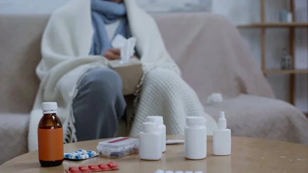 Cropped view of blurred sick man sitting near medicaments on table — Stock Photo