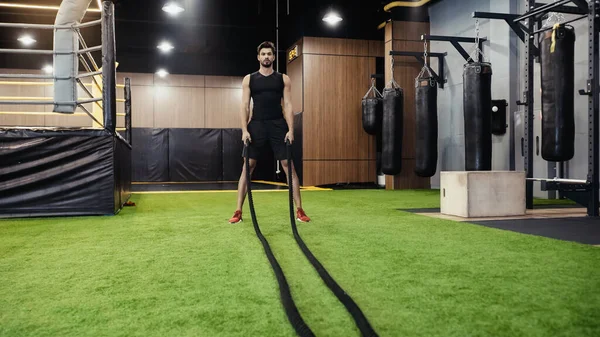 Full length of bearded man working out with battle ropes — стоковое фото