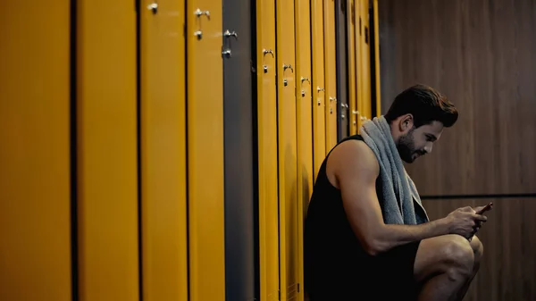 Side view of happy sportsman chatting while using smartphone in locker room — Stock Photo