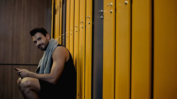 Happy sportsman holding smartphone in locker room — Stockfoto