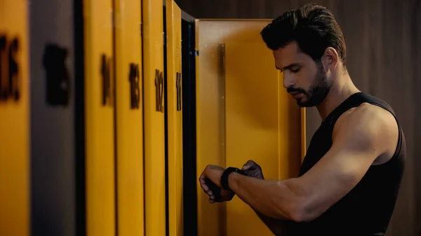 Bearded sportsman looking at smart watch in locker room - foto de stock