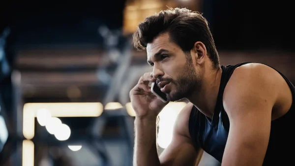 Bearded young sportsman talking on smartphone in gym — Stock Photo