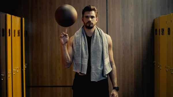 Joven deportista spinning baloncesto en dedo en vestuario - foto de stock