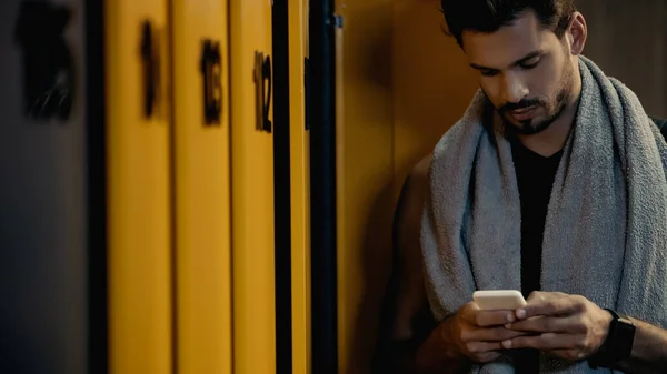 Bearded sportsman messaging on smartphone in locker room — Photo de stock