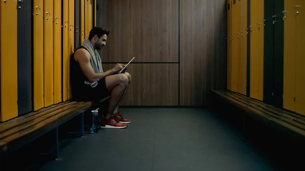 Sportsman sitting on bench and using digital tablet in locker room — Photo de stock