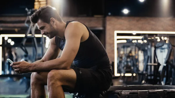 Happy sportsman using smartphone while sitting on car tire — Foto stock