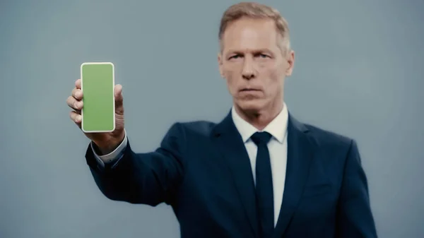 Smartphone with green screen in hand of blurred businessman isolated on grey — Stock Photo