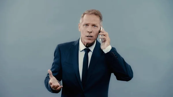 Mature businessman talking on smartphone and looking at camera isolated on grey — Stock Photo