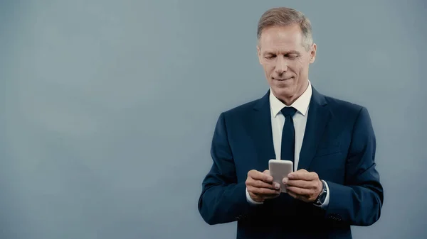 Homme d'affaires mature souriant utilisant un téléphone mobile isolé sur gris — Photo de stock