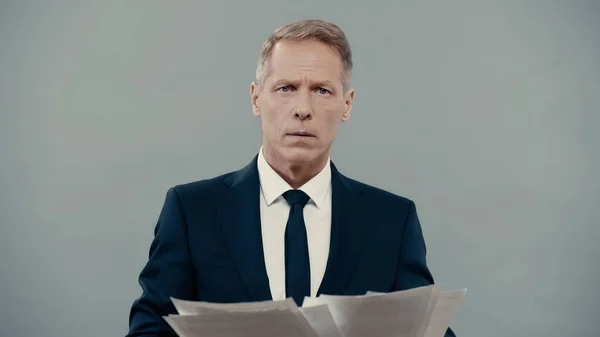 Mature businessman holding papers and looking at camera isolated on grey — Fotografia de Stock