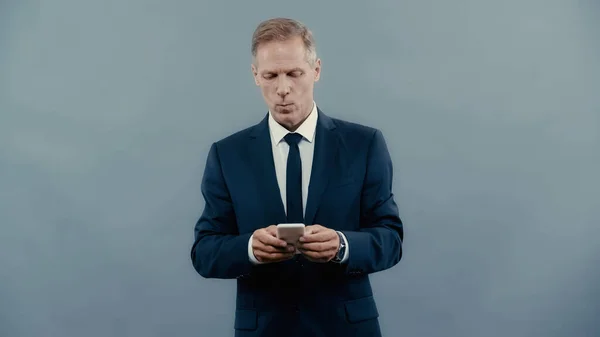 Homme d'affaires mature en costume à l'aide d'un téléphone cellulaire isolé sur gris — Photo de stock