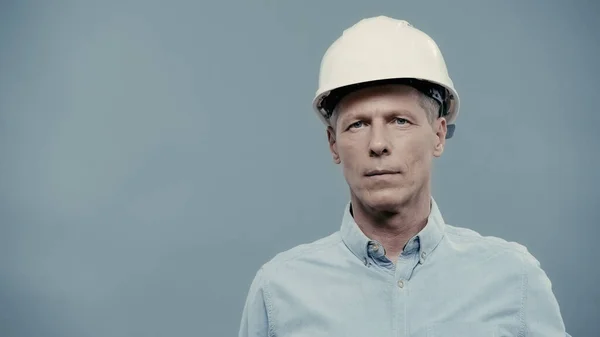 Mature engineer in hardhat looking at camera isolated on grey — Foto stock