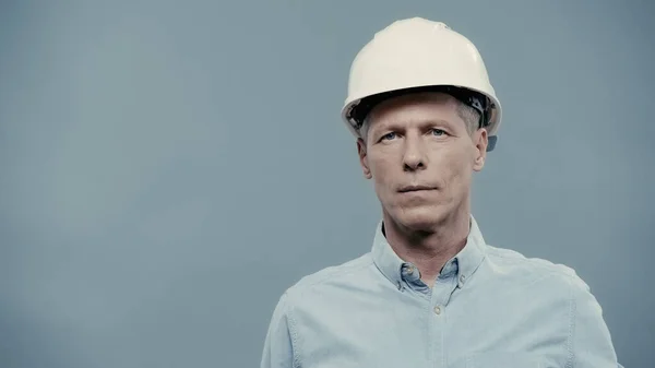 Mature engineer in hardhat looking at camera isolated on grey — Stockfoto