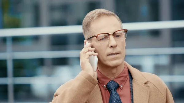Бізнесмен середнього віку в пальто розмовляє на мобільному телефоні на відкритому повітрі — стокове фото