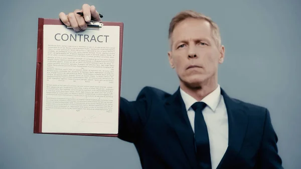 Contract on clipboard in hand of blurred businessman isolated on grey — Stock Photo